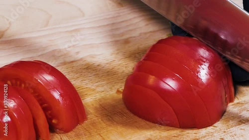 Cutting tomatoes on a cutting board. Close-up. Slow motion. Focus in. Female hands cut the tomato into slices.