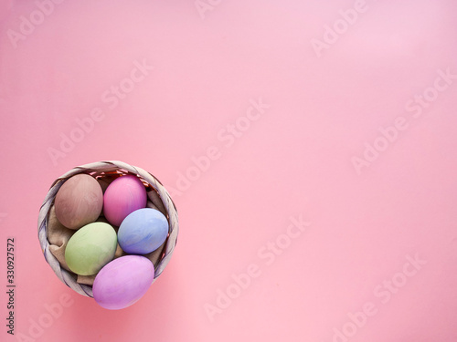 Flat lay composition of Happy Easter holiday concept. Colorful pastel egg in basket on pink background. Copyspace, top view.