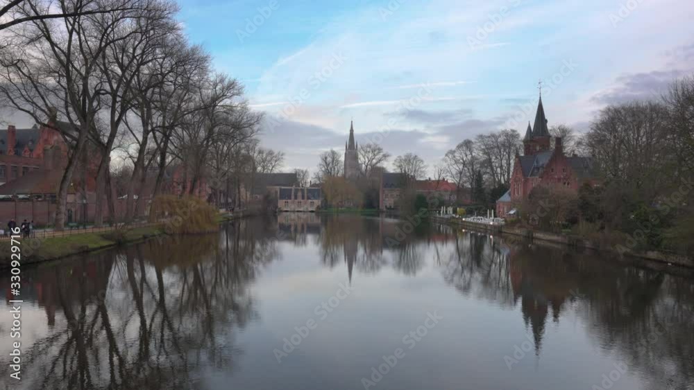 The Tranquil Lake Of Love At The Minnewaterpark In Bruges, Belgium Surrounded By Bare Trees Under The Blue Sky - Wide Shot The Tranquil Lake Of Love At The Minnewaterpark In Bruges, Belgium Surrounded By Bare Trees Under The Blue Sky - Wide Shot