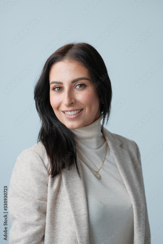 Portrait of a smiling mid-aged business woman in a light milk-colored trouser suit and turtleneck against a light wall. Portrait of a smiling mid-aged business woman in a light milk-colored trouser suit and turtleneck against a light wall.