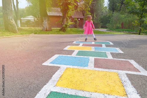 Little girl in a pink dress playing hopscotch on playground outdoors, children outdoor activities photo