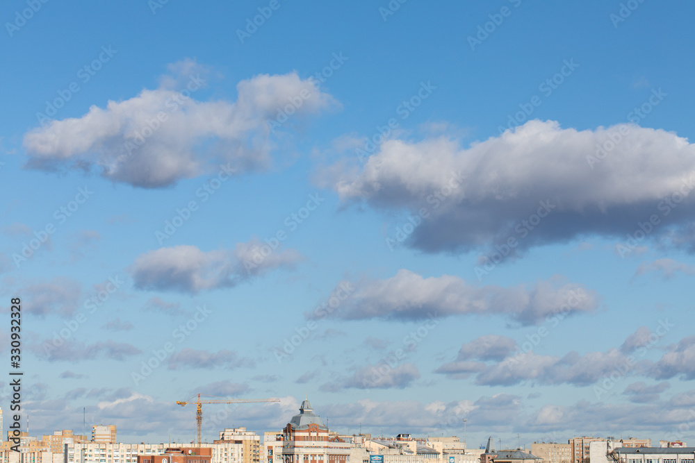tops of city roofs and construction crane over blue cloudy sky.