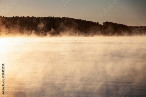 Fog rises over the water of a forest lake. photo