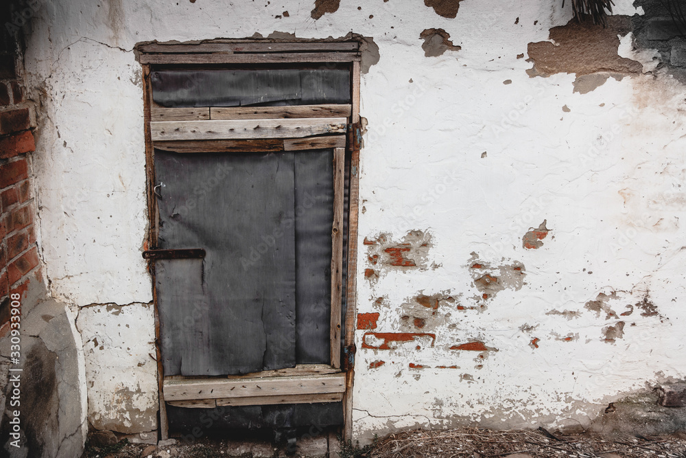 Old white wall of a house with peeling paint and an old closed door. Decrepit building.