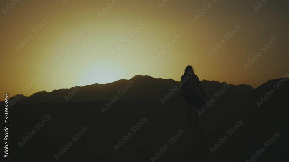 Silhouette of beautiful young woman walk at sunset in desert. Female going through the desert, dunes, wind blowing, slow motion, 4k Silhouette of beautiful young woman walk at sunset in desert. Female going through the desert, dunes, wind blowing, slow motion, 4k