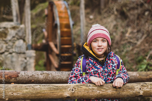 Portrait of little girl on hiking forest trip and watermill.