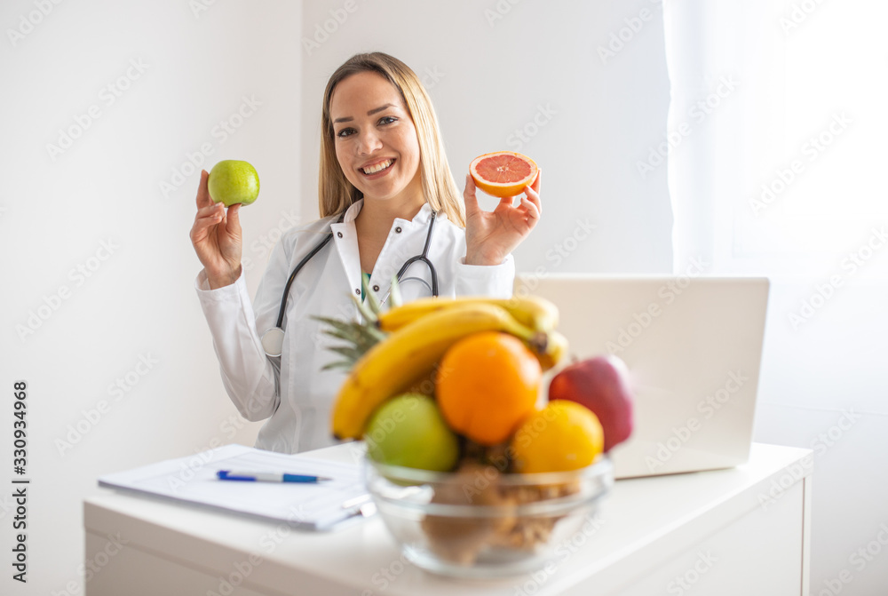 Female nutritionist with fruits working at her desk. Smiling nutritionist in her office, she is showing healthy vegetables and fruits, healthcare and diet concept. 