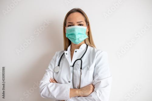 Confident doctor standing arms crossed. Confident young woman doctor. Intern Doctor Young pretty woman in white clothes with medical mask posing.