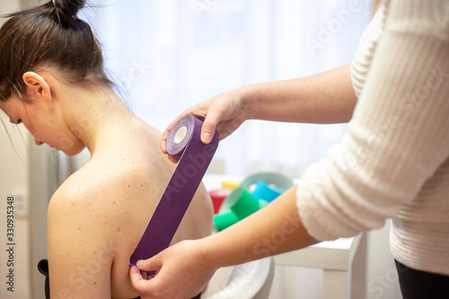 Professional physical therapist applying tape on patients shoulder, kinesiotaping concept photo