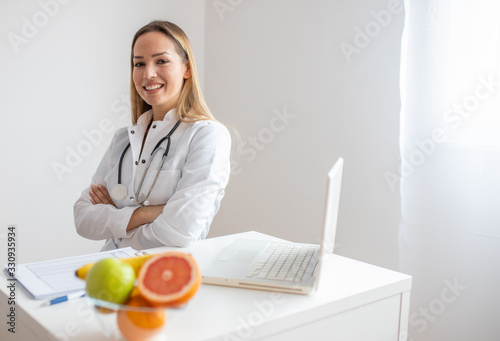 Female nutritionist with fruits working at her desk. Smiling nutritionist in her office, she is showing healthy vegetables and fruits, healthcare and diet concept. 