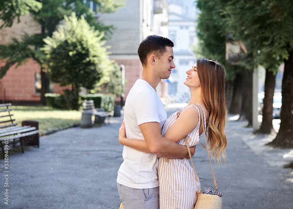 Young couple in love walking on small alley holding hands. Pretty blond woman, wearing stripy short overall and brunette man in white t-shirt and blue shorts on romantic date. Relationship. Vacation. Young couple in love walking on small alley holding hands. Pretty blond woman, wearing stripy short overall and brunette man in white t-shirt and blue shorts on romantic date. Relationship. Vacation.