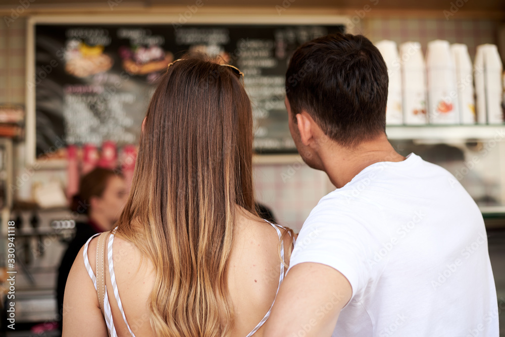 Young couple in love standing at counter desk ordering belgian waffles and coffee for breakfast in the morning. Blond woman and brunette man, wearing white clothes in coffee shop on romantic date. Young couple in love standing at counter desk ordering belgian waffles and coffee for breakfast in the morning. Blond woman and brunette man, wearing white clothes in coffee shop on romantic date.
