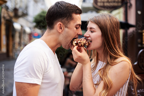 Romantic couple on date eating tasty belgian waffle with chocolate and caramel. Young blond woman, feeding brunette man with yummy desert in summer in the morning. Nutritious breakfast, snack.