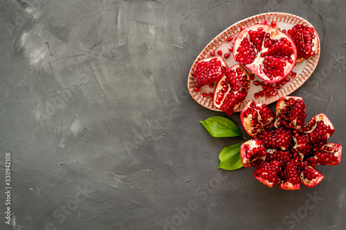 Juicy pomegranate with seeds on plate on grey table top-down copy space