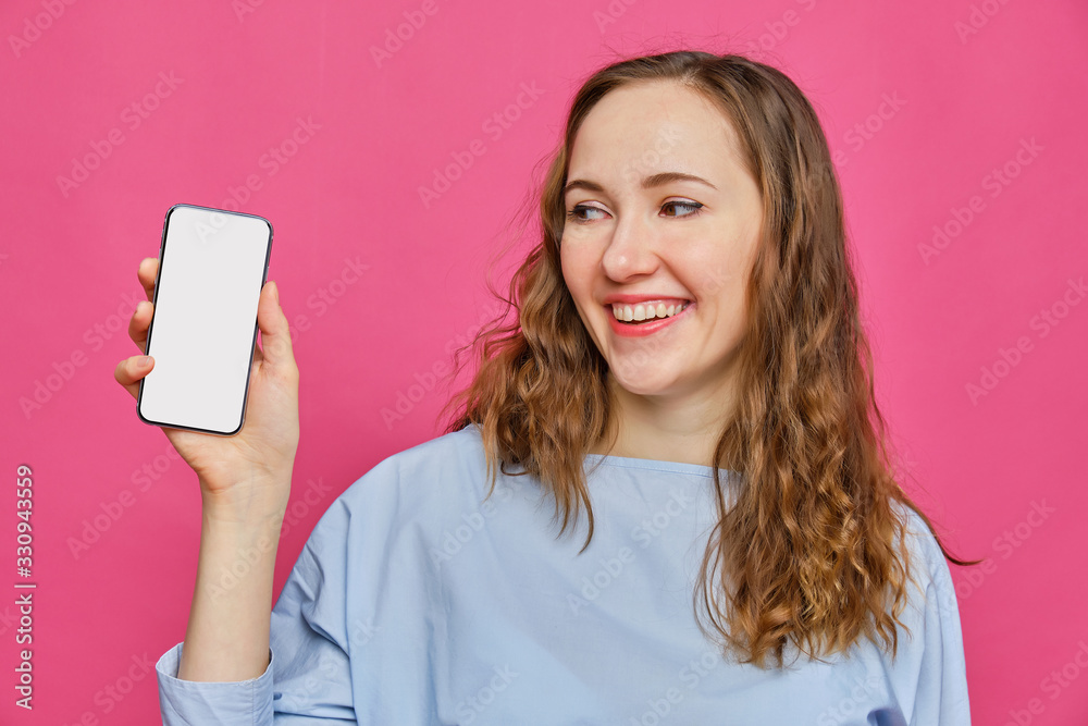 Stylish caucasian girl in a pale blue t-shirt holds a smartphone in his hand and looks at it on a pink background. Copy space. Stylish caucasian girl in a pale blue t-shirt holds a smartphone in his hand and looks at it on a pink background. Copy space.