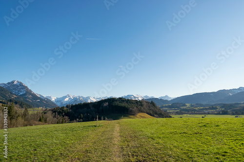 Blick über die saftig grünen Wiesen bis zu den Bergen. Der Himmel ist blau. © Tina Rabus