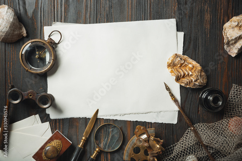 Old fashioned flat lay with letters writing accessories on dark wooden background. White sheets, pen, signet, package, ink. Vintage style, steampunk, gaslight concept. Magnifying glass and compass. photo