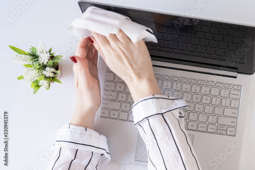 A woman worker cleaning with antivirus wet wipe a laptop and a working office desk before starting work for protect herself from bacteria and virus.