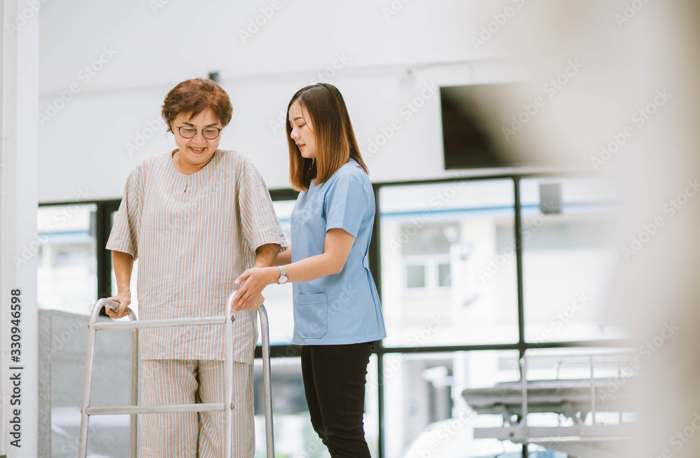 young physical therapist helping senior patient in using walker during rehabilitation young physical therapist helping senior patient in using walker during rehabilitation