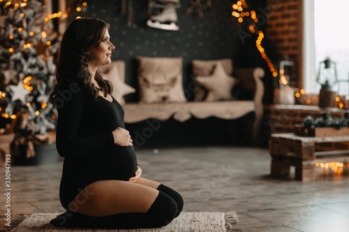 pregnant girl sits on the floor against the background of Christmas decorations