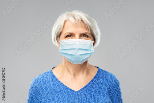 health, safety and pandemic concept - portrait of senior woman wearing protective medical mask for protection from virus over grey background