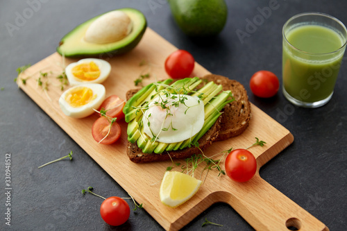 food, eating and breakfast concept - toast bread with sliced avocado, pouched egg, cherry tomatoes and greens on wooden cutting board photo