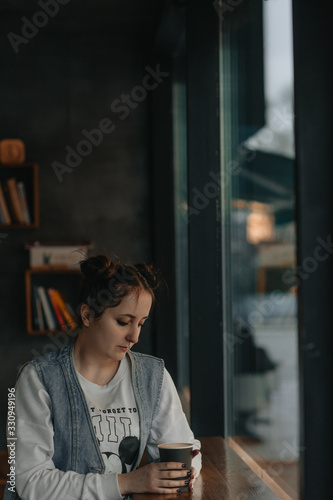 beautiful girl in a coffee shop by the window with a cup of coffee in her hands © Nichita
