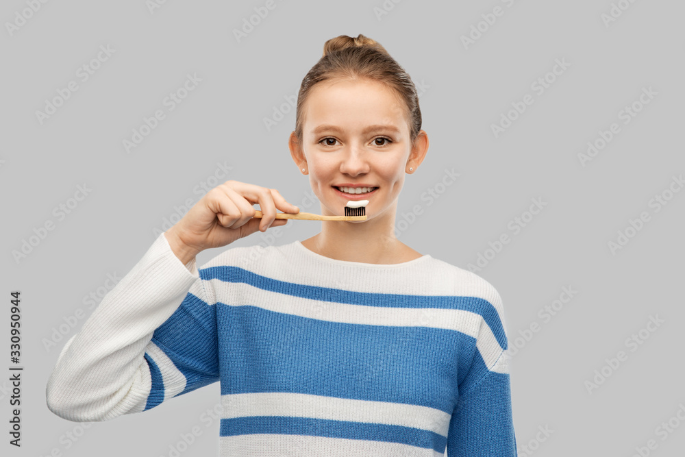 dental care, hygiene and people concept - happy smiling teenage girl in pullover brushing teeth with wooden eco toothbrush over grey background dental care, hygiene and people concept - happy smiling teenage girl in pullover brushing teeth with wooden eco toothbrush over grey background