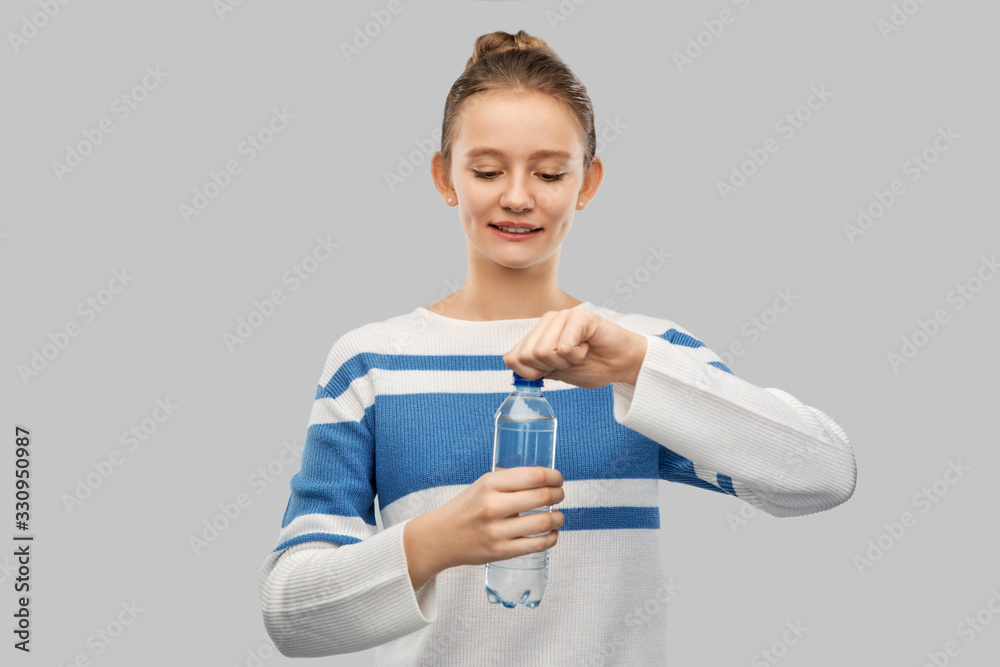 drink, health and people concept - happy smiling teenage girl in pullover opening bottle of water over grey background drink, health and people concept - happy smiling teenage girl in pullover opening bottle of water over grey background