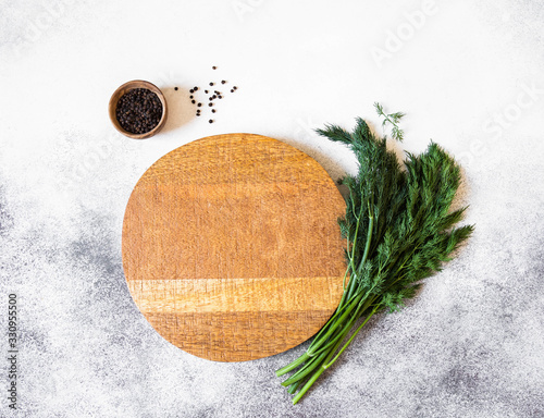 Wood round cutting board, spices in small wood bowl and fresh dill on a gray background. Top view. Copy space