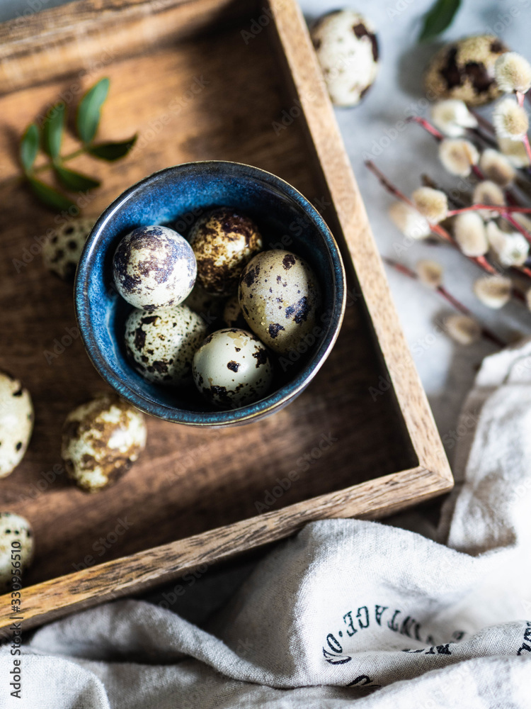 Easter composition with eggs in blue cup on wood tray with willows and leaves on grey background.
