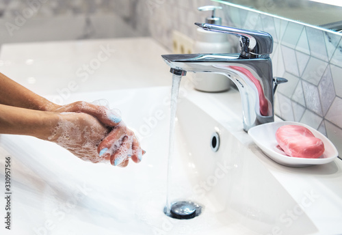 Woman is washing hands with soap and hot water at home bathroom sink. Girl is cleaning hands. Hygiene for coronavirus outbreak prevention. Covid-19 pandemic protection by washing hands frequently