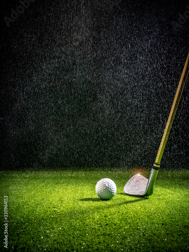 Beam of light in the rain illuminating a golf club and golf ball on the turf