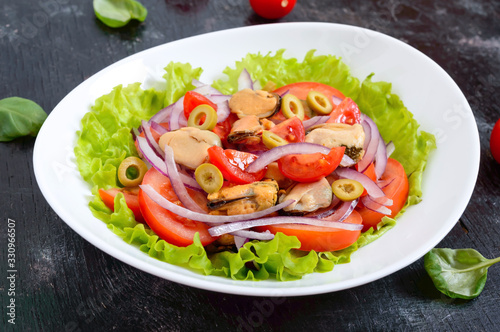 Salad of marinated mussels, fresh tomatoes, red onions, olives in a bowl on a black background