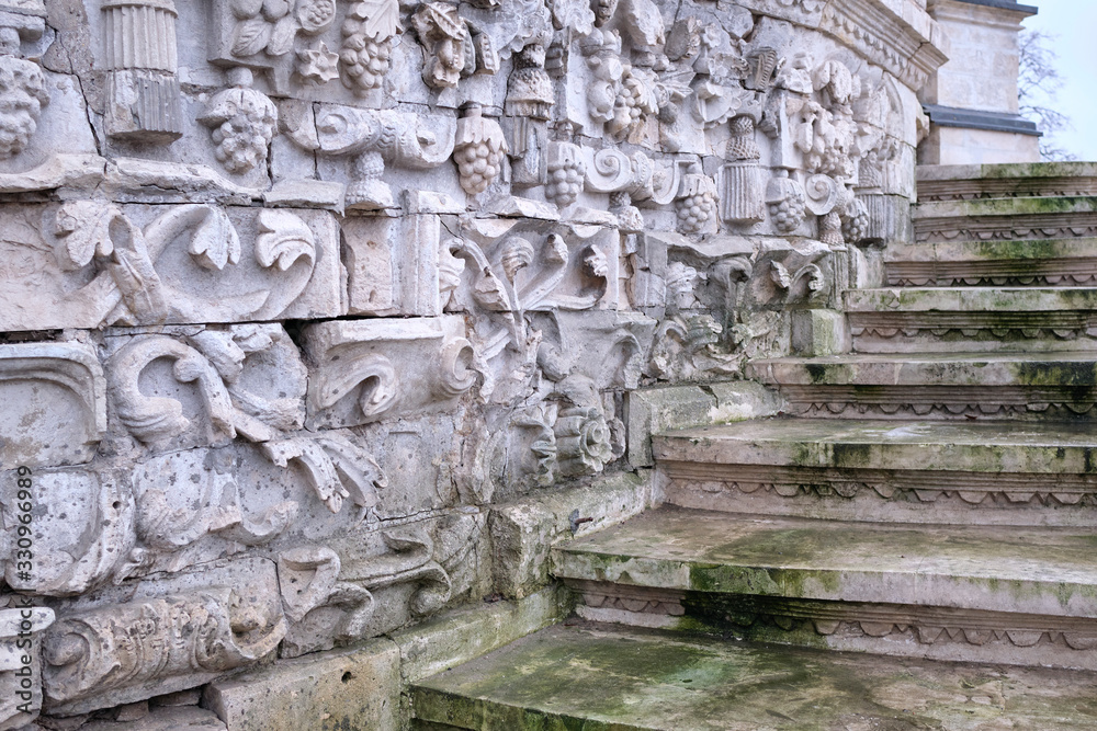 Old steps of white stone covered with mold running along a stone wall with bas-relief.