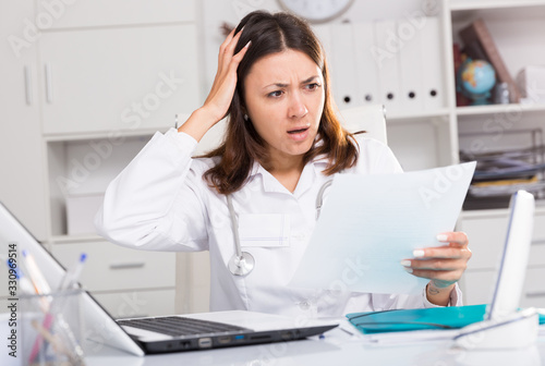 Upset practicioner girl is working with documents and laptop