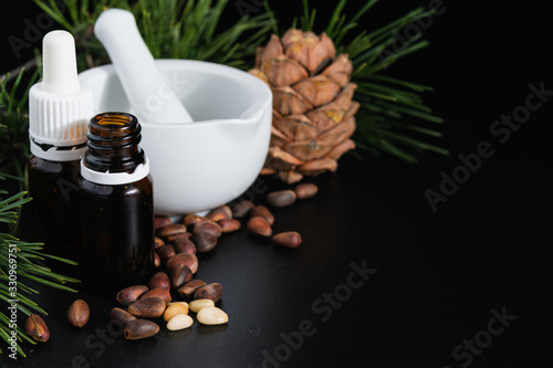 natural production concept, pine cone with nuts, glass bottle and mortar on a black background