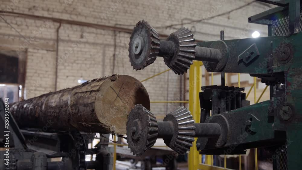 Worker corrects a log on a conveyor belt. Processing of round timber logs for building wooden house. Removing bark from logs using a machine. Pattern of logs. Woodworking factory. Worker corrects a log on a conveyor belt. Processing of round timber logs for building wooden house. Removing bark from logs using a machine. Pattern of logs. Woodworking factory.