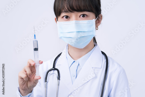 Doctor holding syringe with face mask  concept of young female physican injects coronavirus  COVID-19 vaccine on white background  close up  copy space