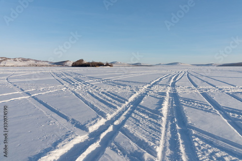 Beautiful geometric patterns from the wheels of cars were imprinted on the snowy plain of the lake against the shore.