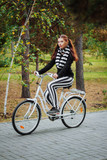 A young, attractive woman rides a white bike in the evening in an autumn park.