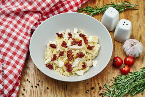 Italian homemade tagliatelle with dried tomatoes, chicken and mozzarella in a beige pial on a wooden background. Tasty pasta. Copy space