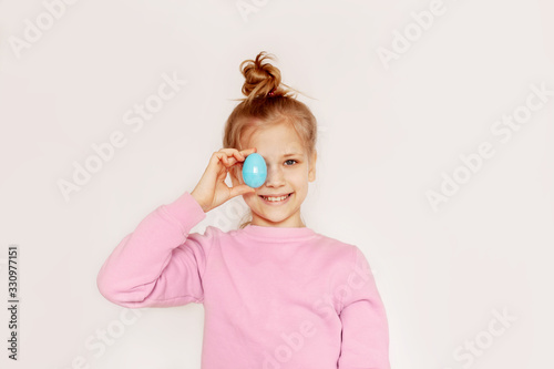 Cute happy girl holding an Easter egg in her hands. Portrait of a child on a light background with space for text