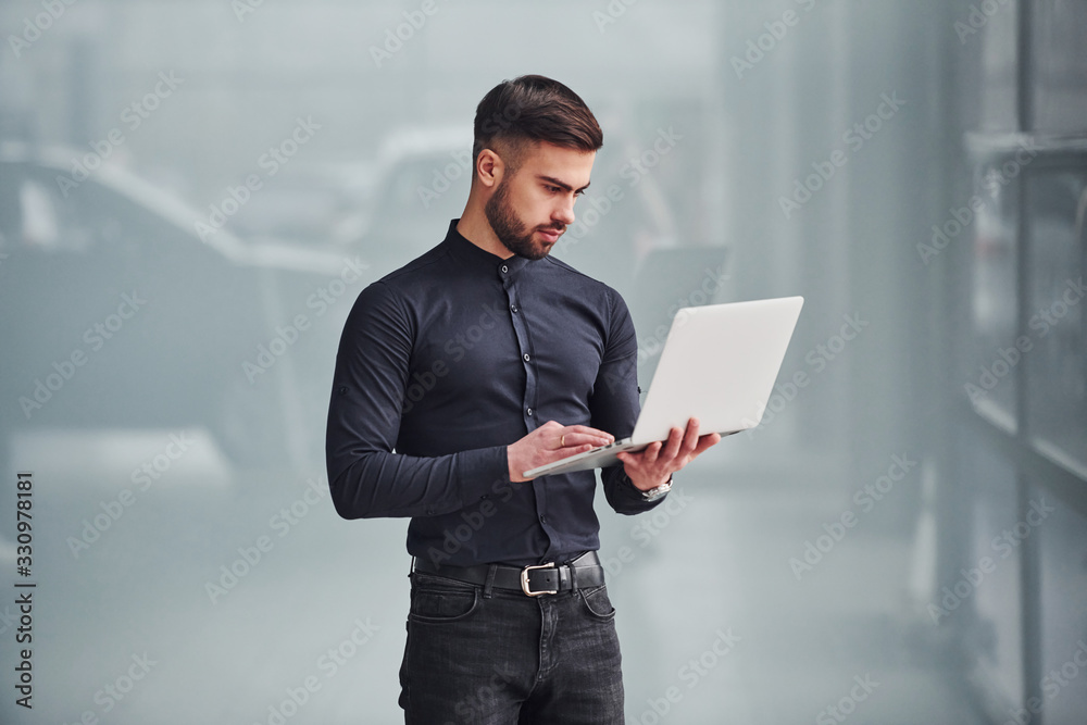 Young bearded guy in elegant clothes standing indoors against grey background Young bearded guy in elegant clothes standing indoors against grey background