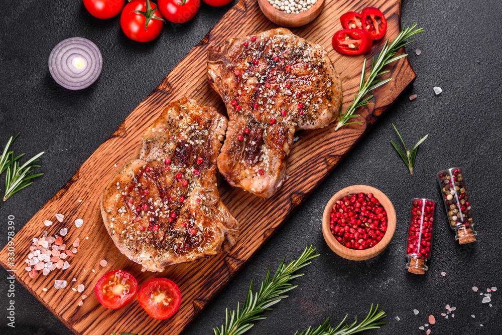 Fresh delicious juicy steak on the bones with vegetables and spices against a dark background Fresh delicious juicy steak on the bones with vegetables and spices against a dark background