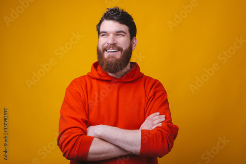 Young cheerful bearded man smiling and looking aside with crossed arms