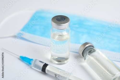 Vials, syringe and surgical mask on light background. Vaccination and immunization