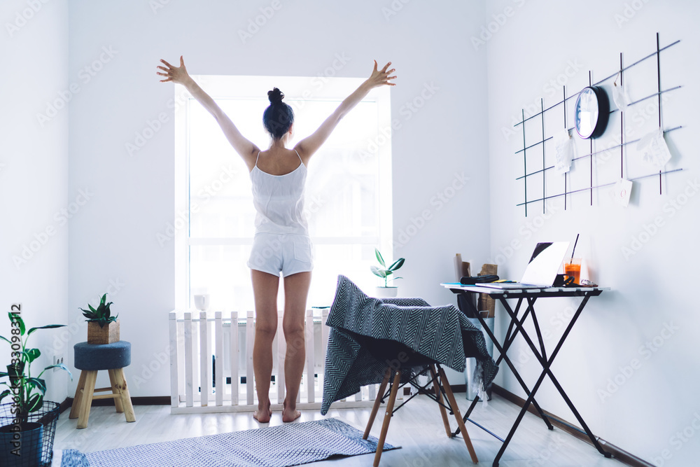 Positive woman enjoying morning while standing by window - obrazy, fototapety, plakaty 