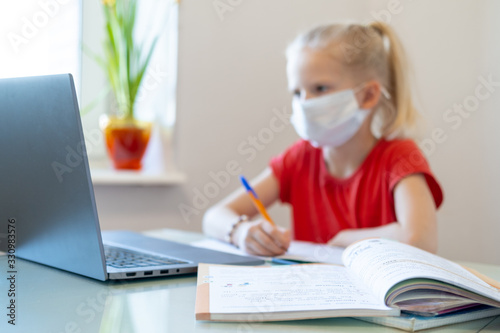 Distance learning online education. Blurred sickness schoolgirl in medical mask studying at home, looking at laptop notebook and doing school homework. coronavirus quarantine. photo