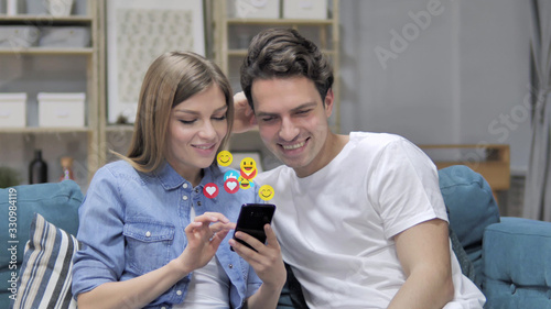 Smiling Young Couple Using Smartphone, Flying Smileys, Emojis and Likes